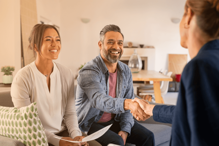 A happy couple shaking hands and signing a contract with an advisor.