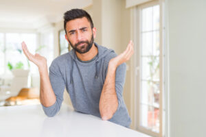 Man at kitchen table with hands in air confused